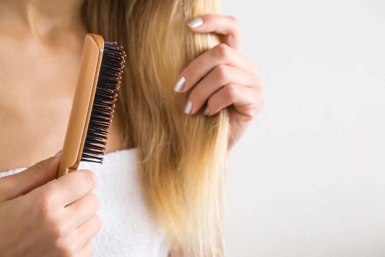 Woman's hand brushing blonde hair. Cares about a healthy and clean hair. Beauty salon. Empty place for a text on the gray background