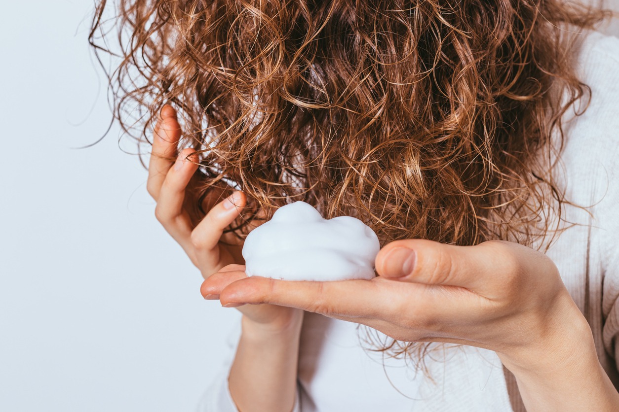 Woman's hands apply styling mousse to her curly hair